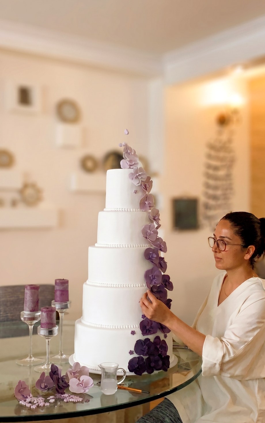 CakeHub Toronto artisan hand-decorating a 5-tier white wedding cake with cascading purple orchids
